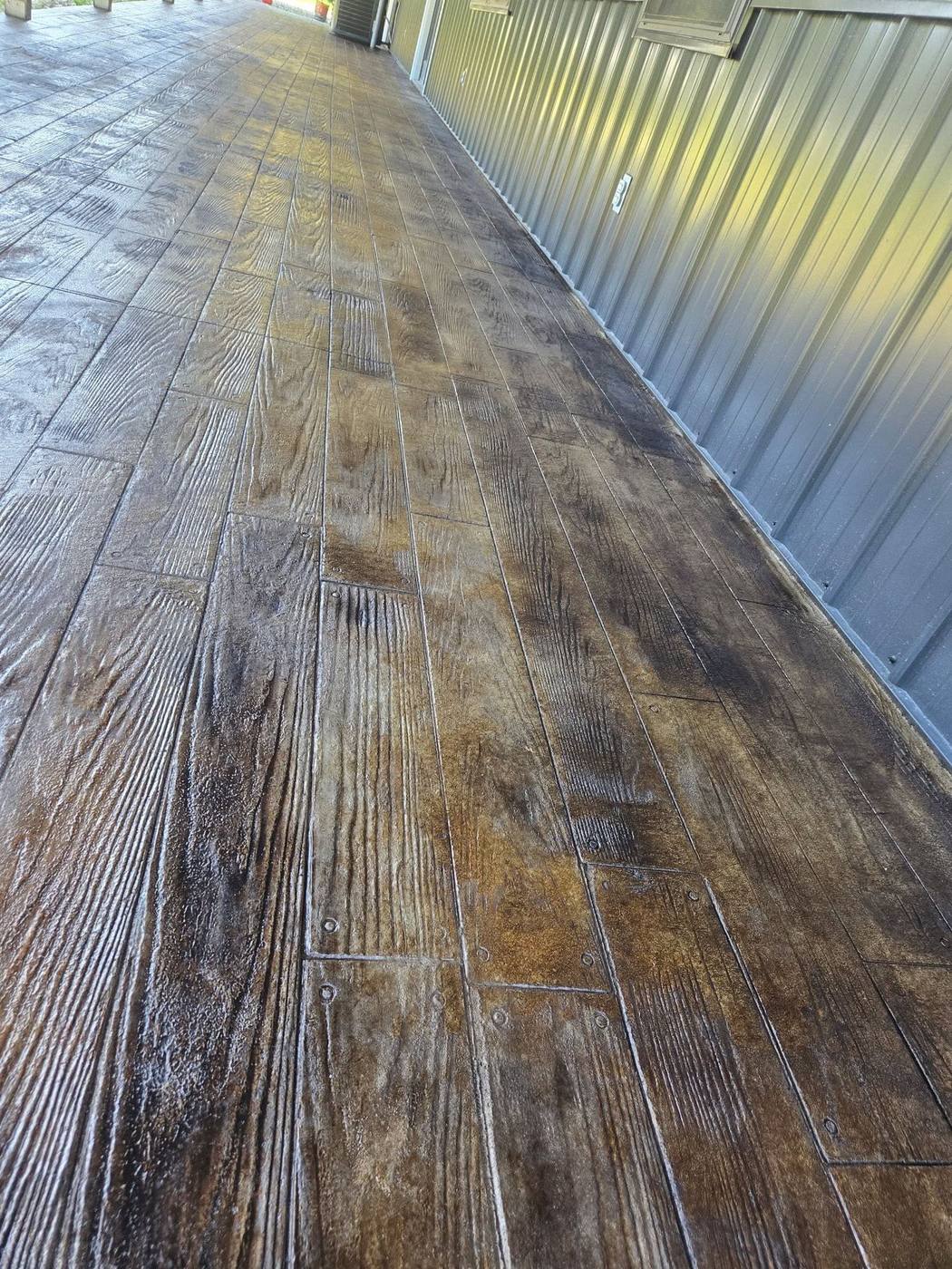 Wood-plank stamped walkway in raking light along a metal building