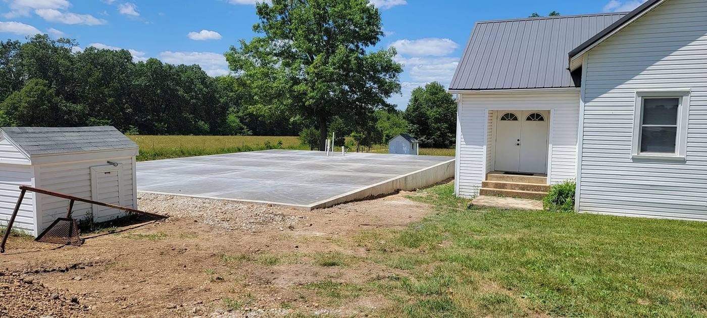 Raised slab foundation poured beside a white farmhouse